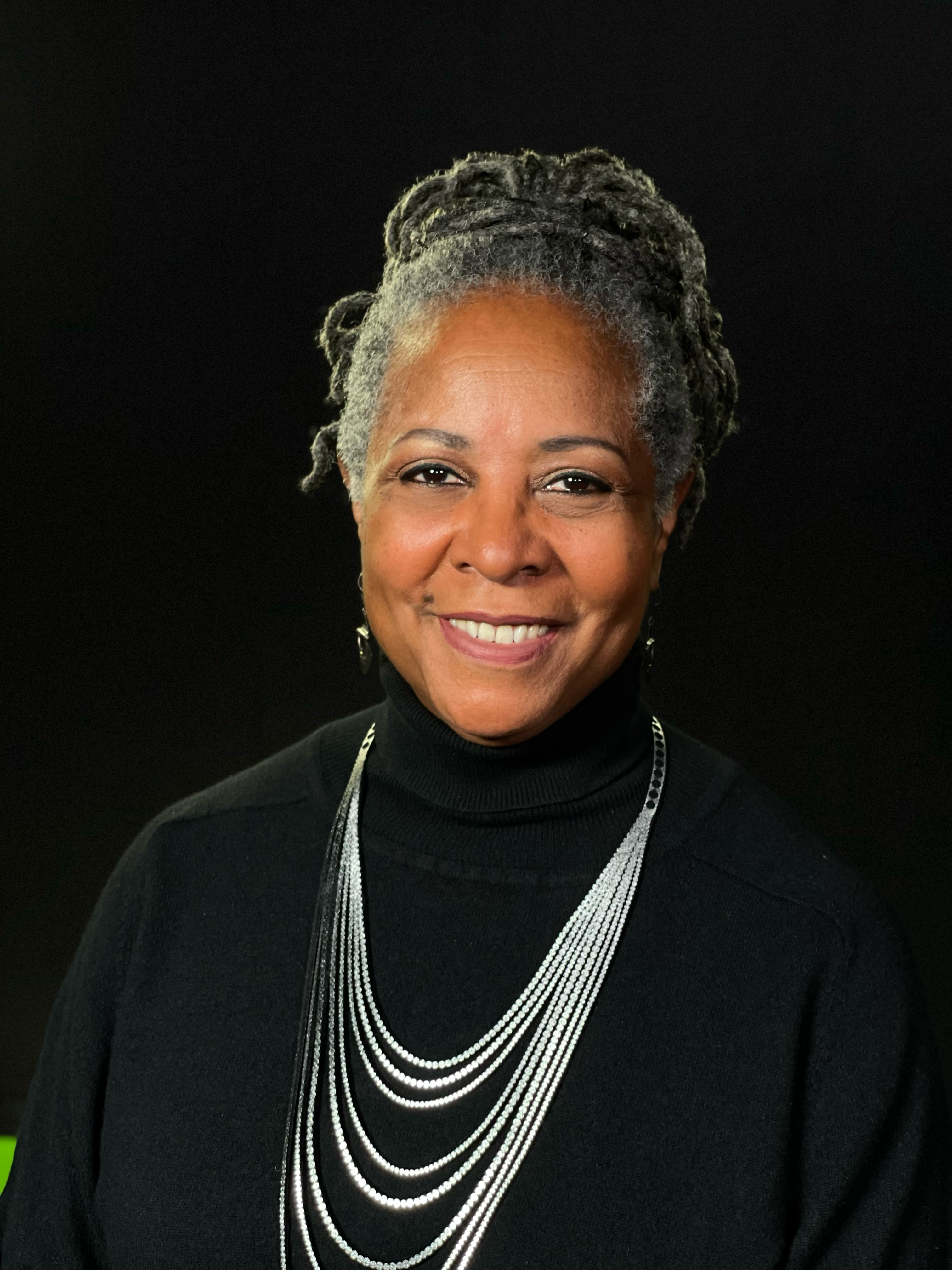 Photo of Dr. Robin Denise Johnson, a Black woman smiling at the camera, with graying hair, wearing a black turtle neck shirt and a brilliant silver necklace. 