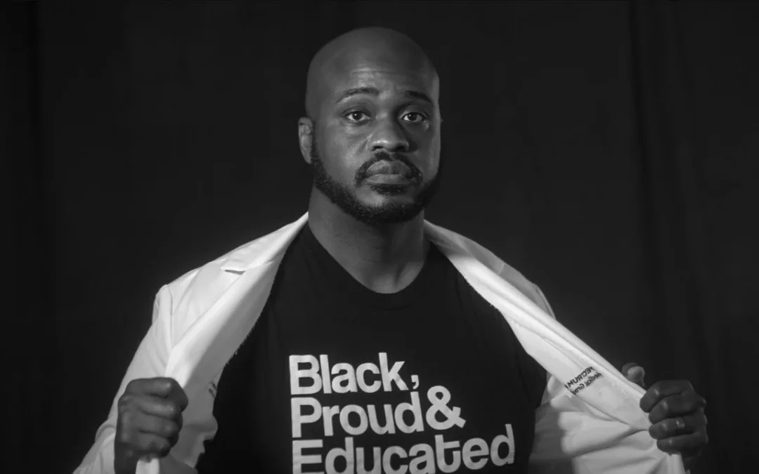 Black man with medical coat open to expose a T-shirt that says "black, proud and educated"